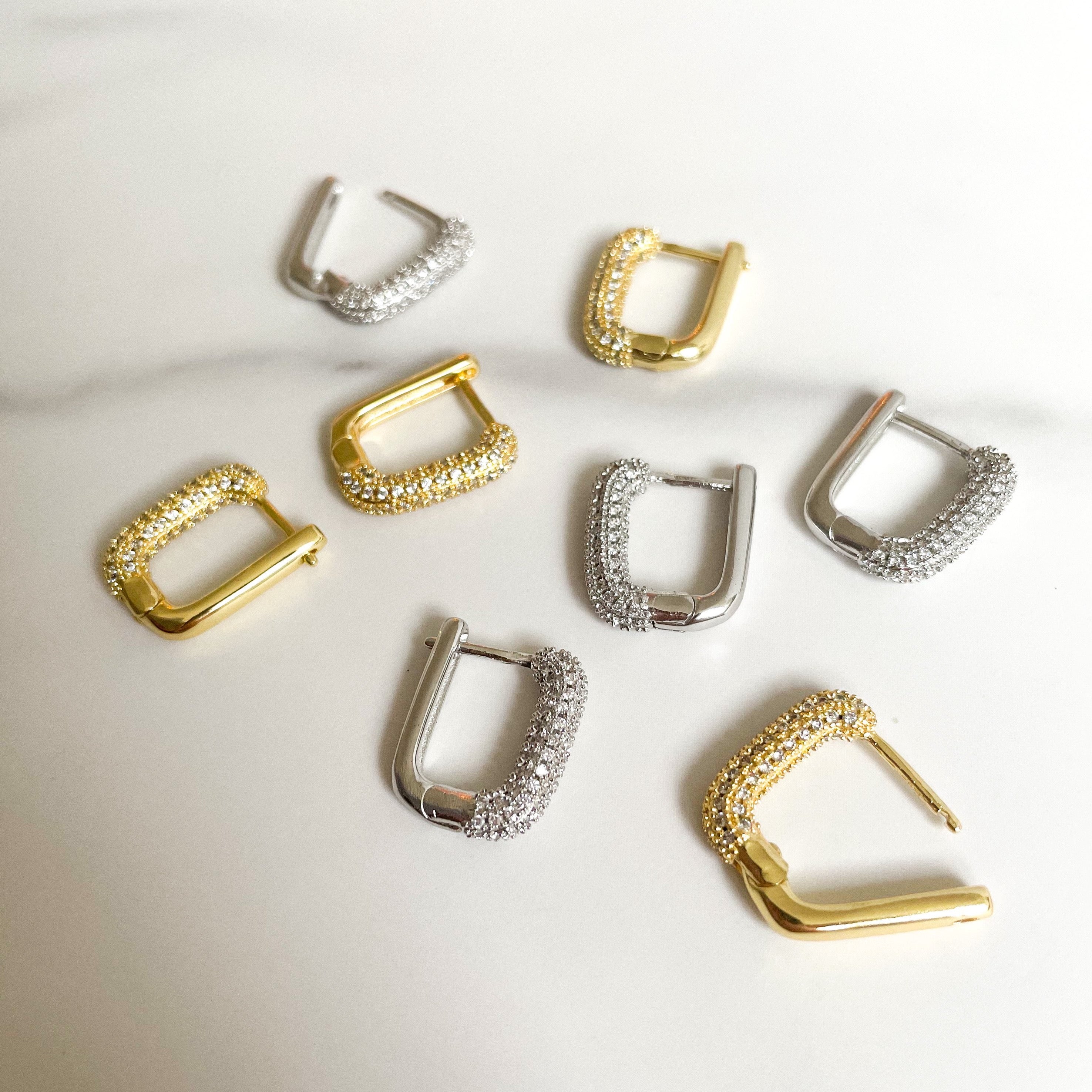 Dit zijn goude en zilvere oorbellen met een rechthoekige vorm. Aan de voorzijde zitten siersteentjes, zirconia diamantjes. de oorbellen zijn gemaakt van gold plated en verkleuren niet, dus stainless steel. Op deze foto zie je de goude en zilvere oorbellen bij elkaar op een martelen achtergrond.