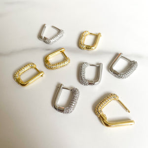 Dit zijn goude en zilvere oorbellen met een rechthoekige vorm. Aan de voorzijde zitten siersteentjes, zirconia diamantjes. de oorbellen zijn gemaakt van gold plated en verkleuren niet, dus stainless steel. Op deze foto zie je de goude en zilvere oorbellen bij elkaar op een martelen achtergrond.